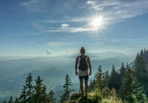 man standing on green grass in front green trees field near mountains